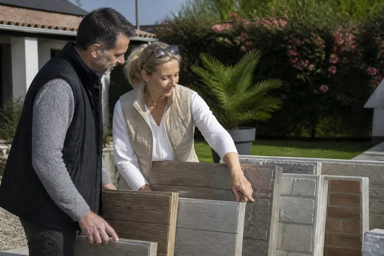 Couple français choisissant des panneaux de cloture-en-beton imitation bois et pierre pour leur jardin.