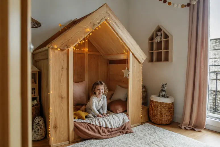 Décoration d'un lit-cabane-bosco avec guirlandes lumineuses et coussins colorés pour un univers enfantin.