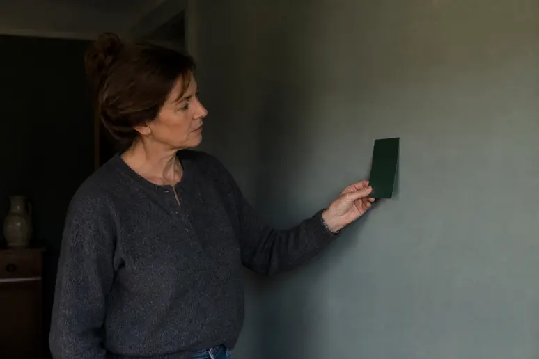 Choisir une couleur pour pièce sombre : femme envisageant un vert émeraude intense pour une ambiance audacieuse.