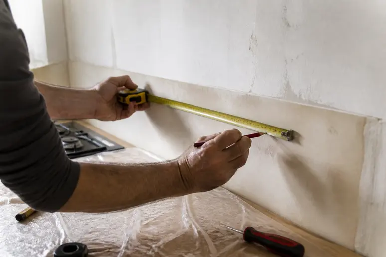 Mains précises mesurant un mur pour la pose d'une crédence de cuisine en carrelage.