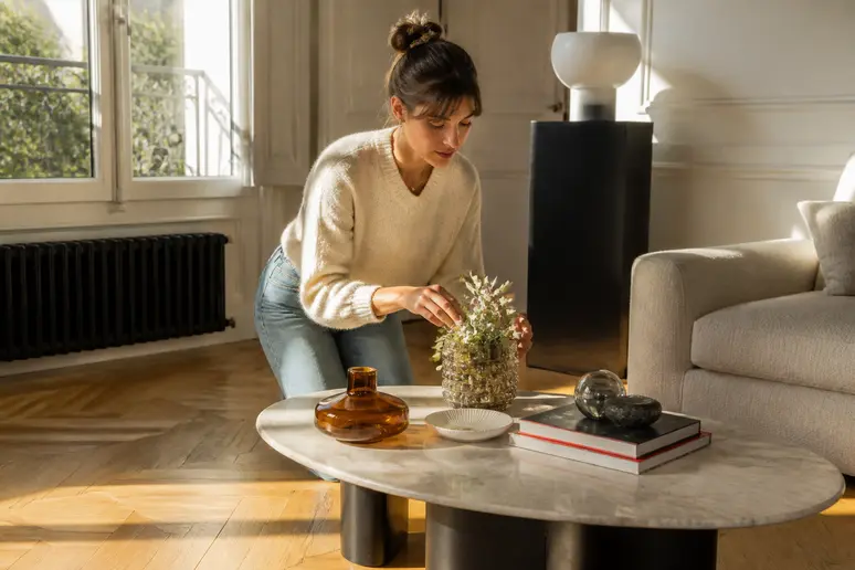 Femme arrangeant des objets sur une table basse, parquets clairs et foncés contrastant.