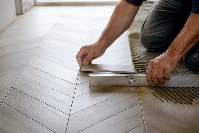 Mains d'un professionnel ajustant la découpe de carreaux pour la pose carrelage en chevron.
