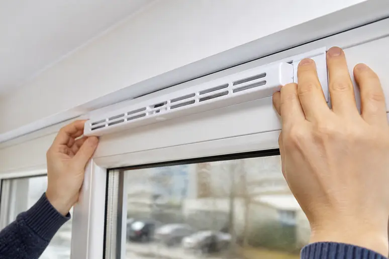 Grille d'aération autoréglable installée sur la traverse supérieure d'une fenêtre PVC.