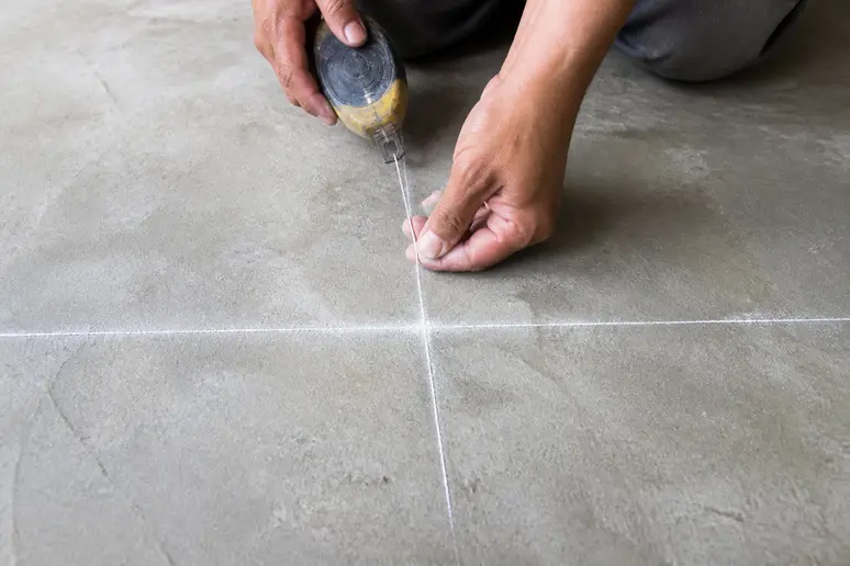 Utilisation d'un cordeau traceur sur une dalle brute pour marquer les axes de référence du carrelage.