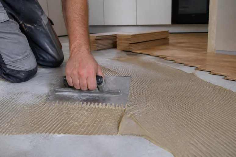 Application de la colle pour parquet en cuisine à l'aide d'une spatule crantée sur la chape.