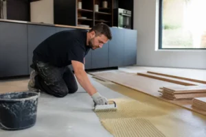 artisan poseur appliquant de la colle sur le sol pour installer un parquet en cuisine