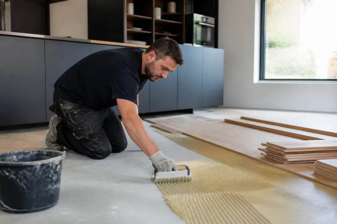 artisan poseur appliquant de la colle sur le sol pour installer un parquet en cuisine