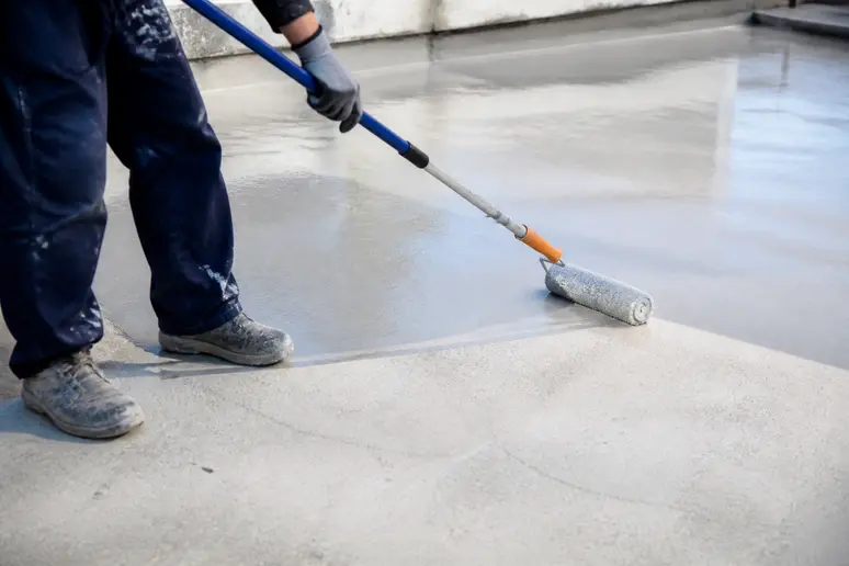 Application d'une résine polyuréthane avec un rouleau sur un sol en béton extérieur