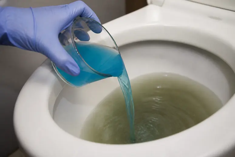 Gants de protection versant un verre de produit détartrant dans la cuvette des WC