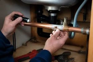 Plombier inspectant une canalisation pour boucher un trou de robinet autoperceur sous un évier