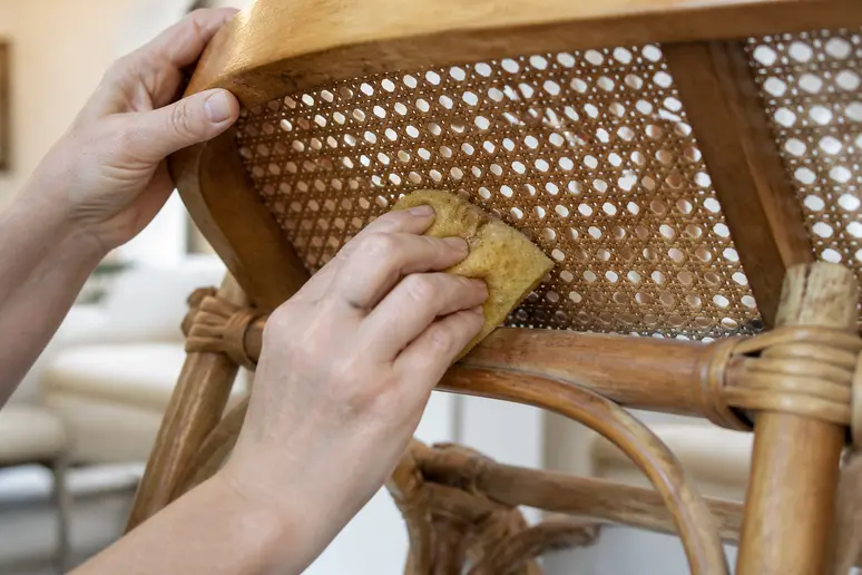 Mains humidifiant l'envers d'un cannage avec une éponge pour retendre le tissage affaissé.