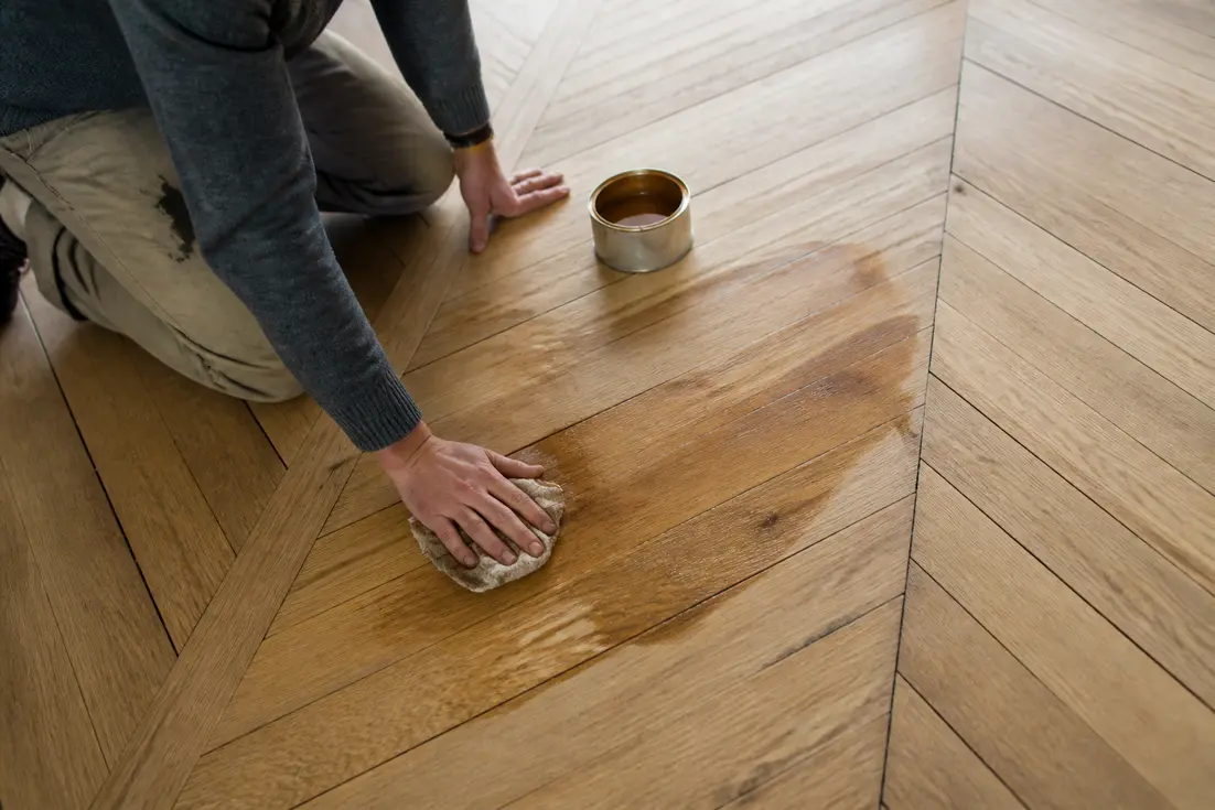 Personne appliquant un cirage pour parquet sur un plancher en bois ancien dans une pièce lumineuse